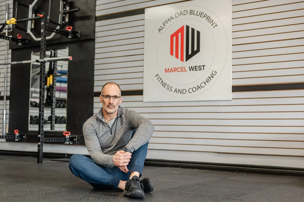 Marcel West seated on the studio floor in front of the MW Fitness and Coaching wall sign
